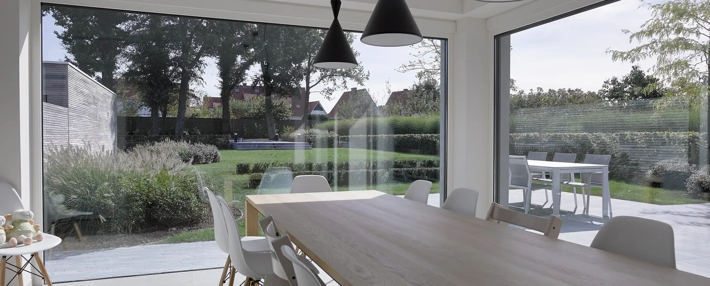 Eetkamer met grote aluminium raampartijen die uitkijken op de tuin