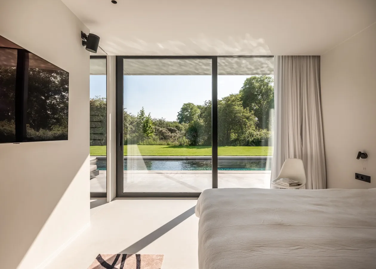 Slaapkamer met een grote aluminium raampartij die uitkijkt op het zwembad en de tuin