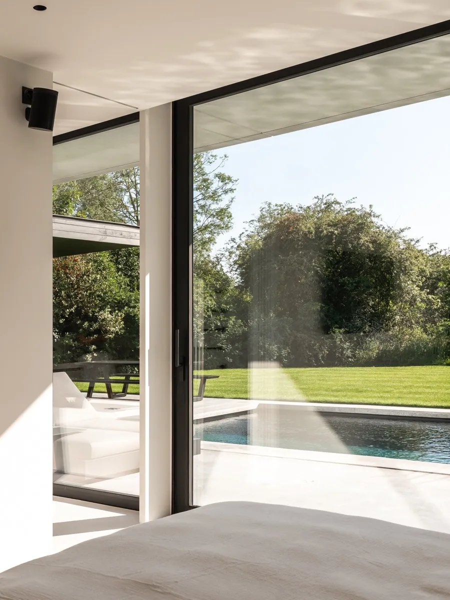 Hoek van de slaapkamer met een hoge aluminium raampartij naar het terras
